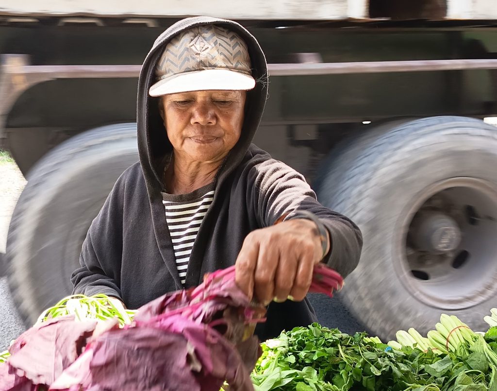 Mama Martina , pedagang sayur mayur di pinggir jalan masuk Tempat Pelelangan Ikan di Oeba, Kota Kupang melepas rindu pada anaknya dengan menatap fotonya yang disimpan dalam telepon seluler. Mama Martina awalnya malu mengetahui anaknya berperilaku layaknya perempuan. Belakangan dia menerimanya. Dok. KatongNTT)